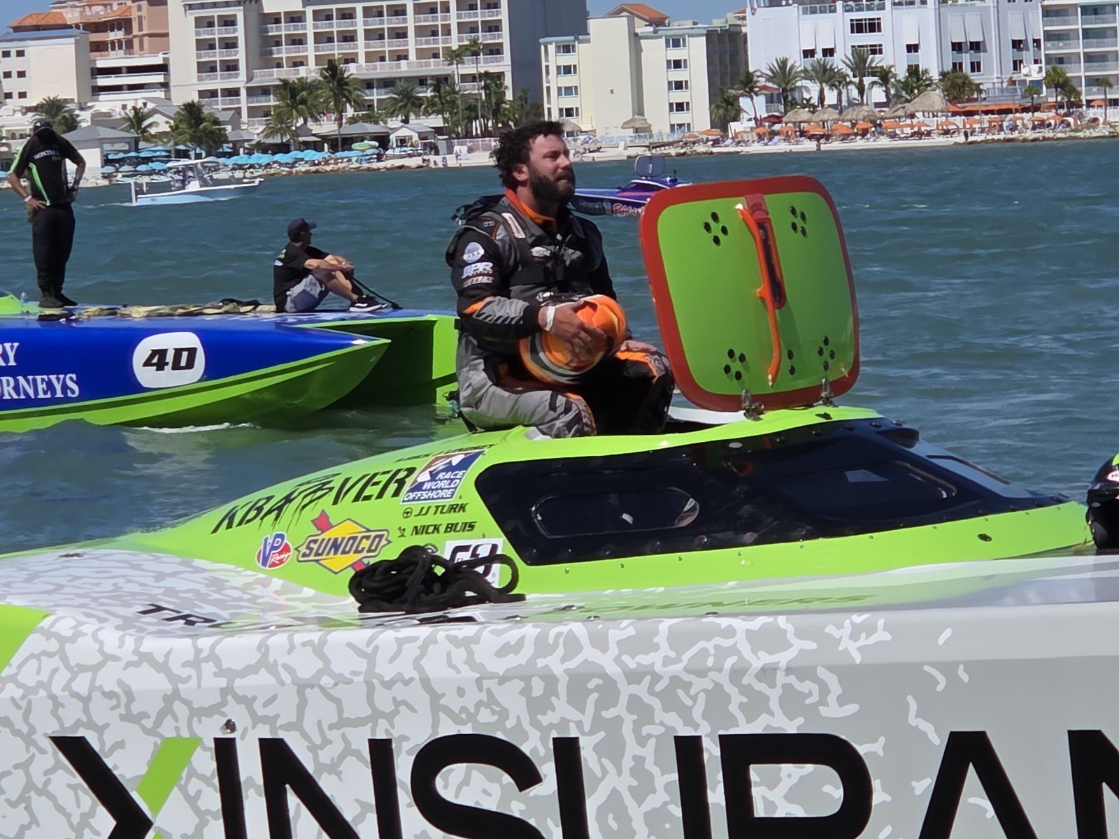 Driver in the cockpit of a green catamaran with XINSURANCE on the deck
