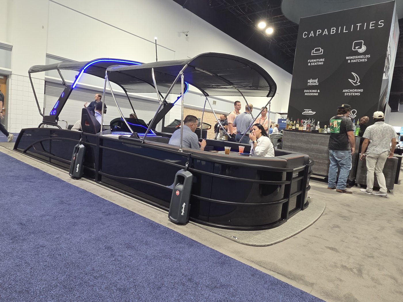 Black luxury pontoon with blue LED bimini beside a Capabilities sign
