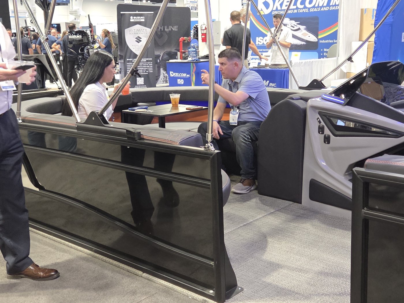 Visitors seated at the table in the black pontoon lounge with Kelcom and Suzuki Marine banners behind